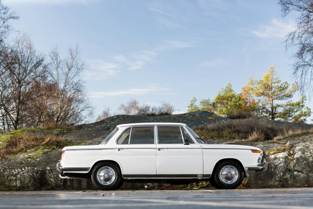 Exteriörbild av en vit BMW 1800, parkerad vid en naturskön plats.