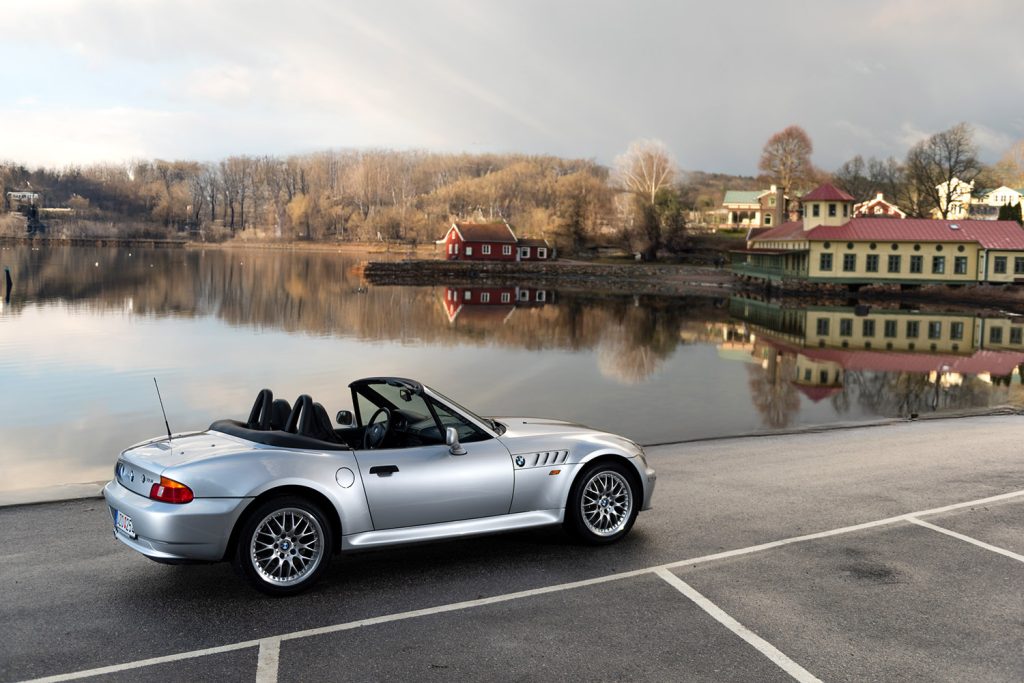 BMW Z3 cabriolet parkerad vid en sjö, med en naturskön bakgrund.