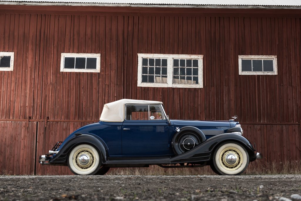 Pontiac cabriolet veteranbil fotograferad framför röd träbyggnad.