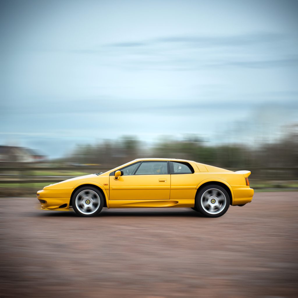 Gul Lotus Elite fotograferad i rörelse på landsväg för auktion.