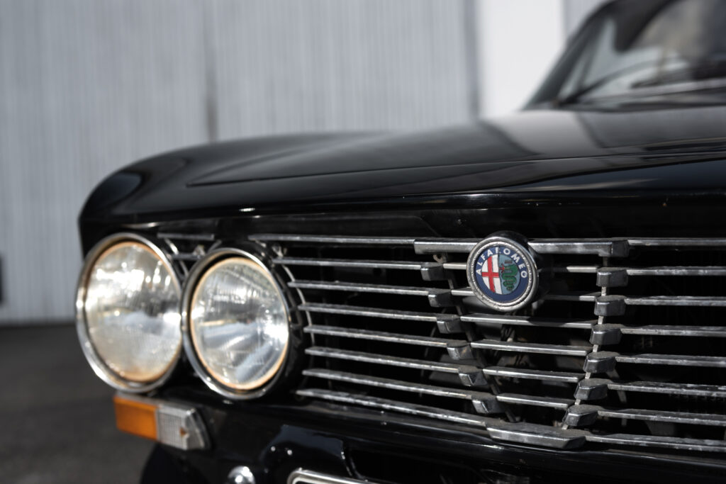 Närbild på Alfa Romeo GTV 2000:s front från 1973 med detaljerad grill och dubbla strålkastare. En tidlös klassiker.