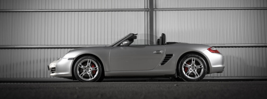 Silverfärgad Porsche Boxster parkerad vid en vägg, utrustad med sportiga sommardäck för optimal prestanda på torra vägar.