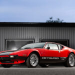 De Tomaso Pantera GTS i röd och svart lack, fotograferad i profil framför industriell byggnad.