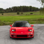 Röd Honda NSX första generationen framifrån på svensk landsväg med uppfällda pop up lampor