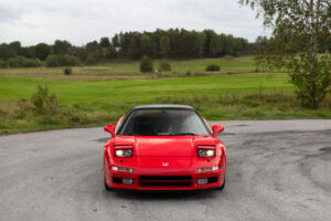 Röd Honda NSX första generationen framifrån på svensk landsväg med uppfällda pop up lampor