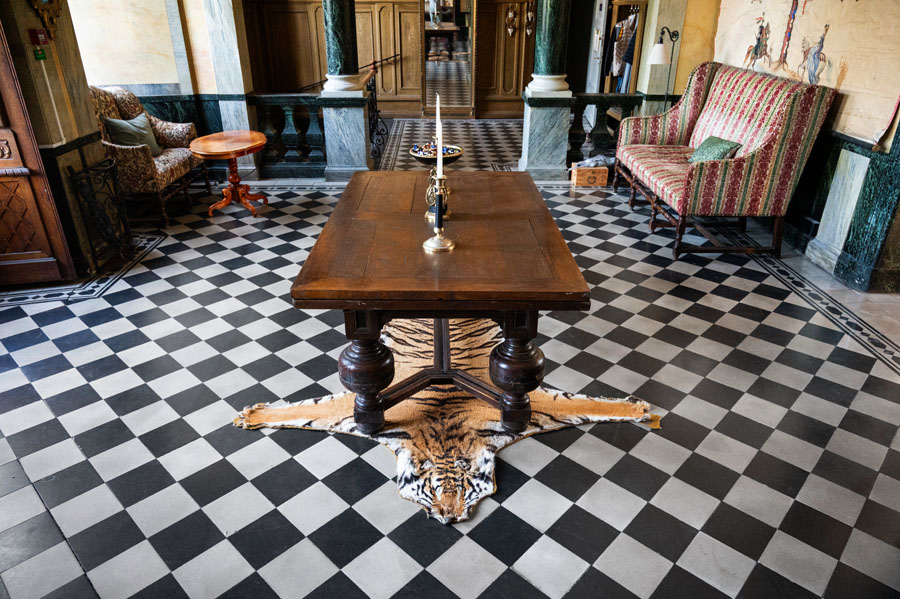 Historisk interiör på Kronovalls slott på Österlen med svartvitt stengolv, antika möbler och konst.