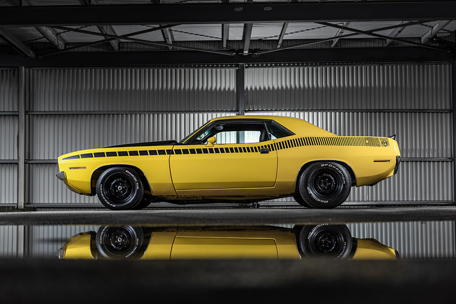 Gul Plymouth ’Cuda fotograferad av Runbox i industrimiljö med spegling i golvet.